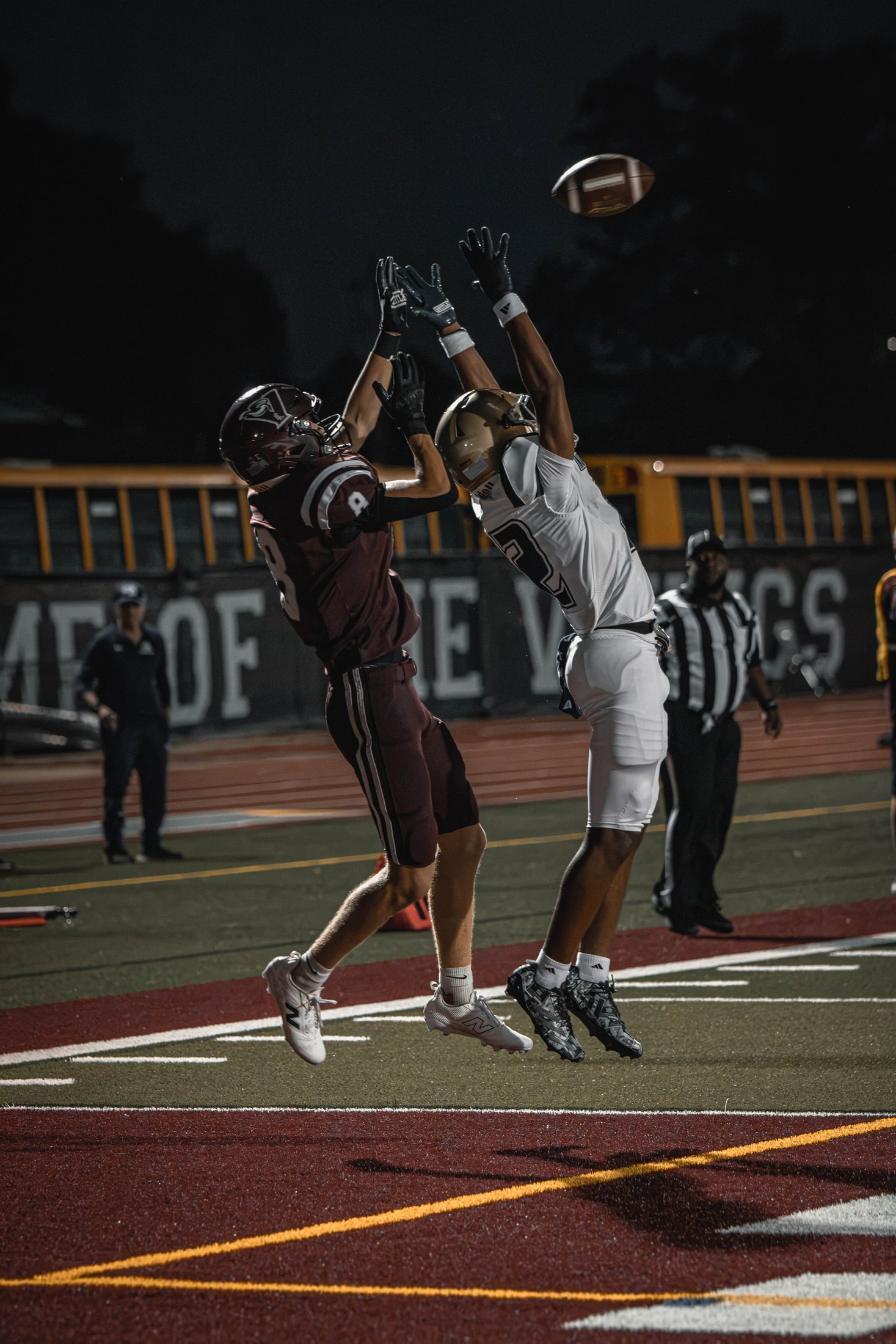 East Lyme receiver and a defender leaping for a contested pass near the sideline at night