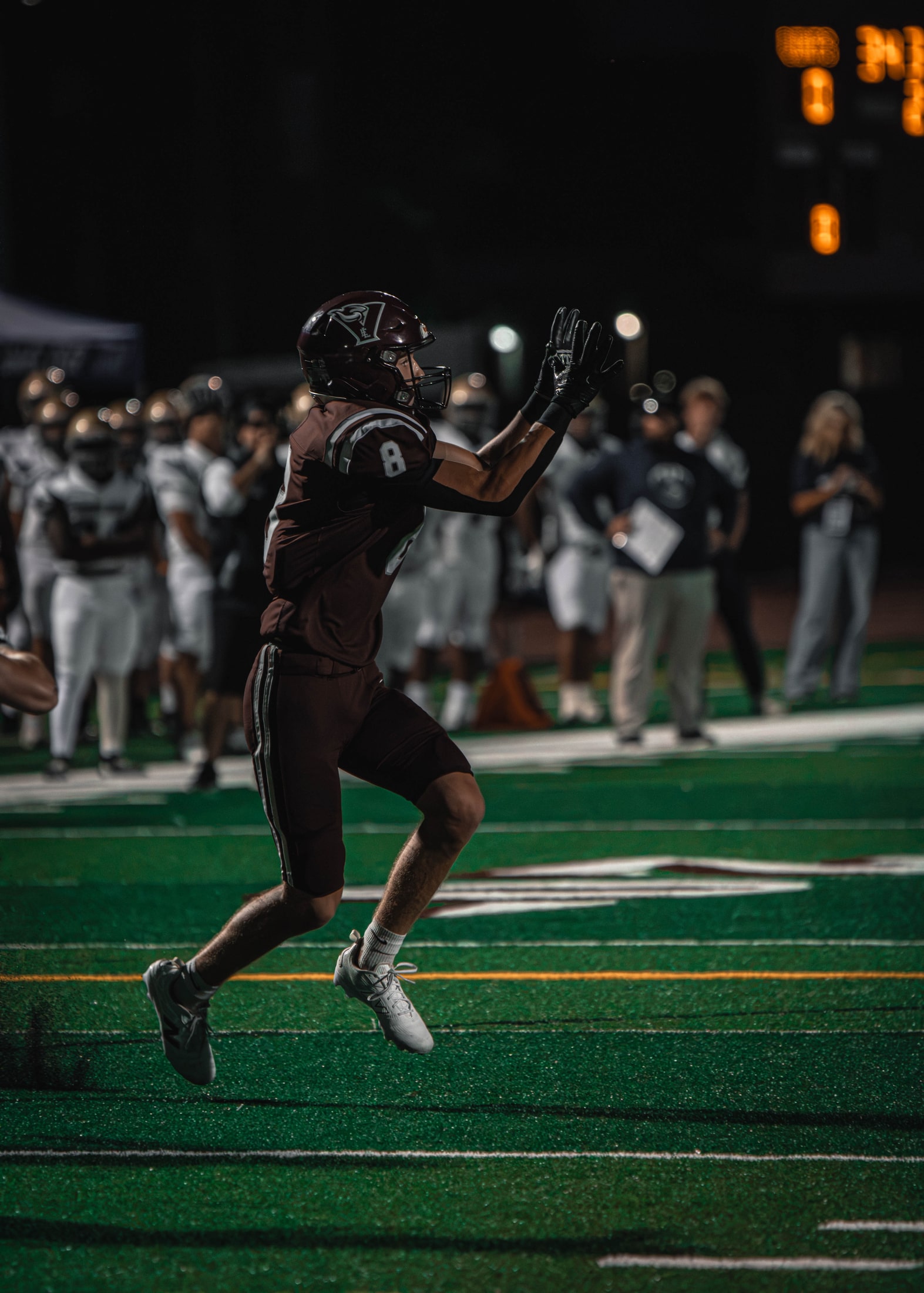 East Lyme number 8 tracking an incoming pass with both hands raised under the stadium lights