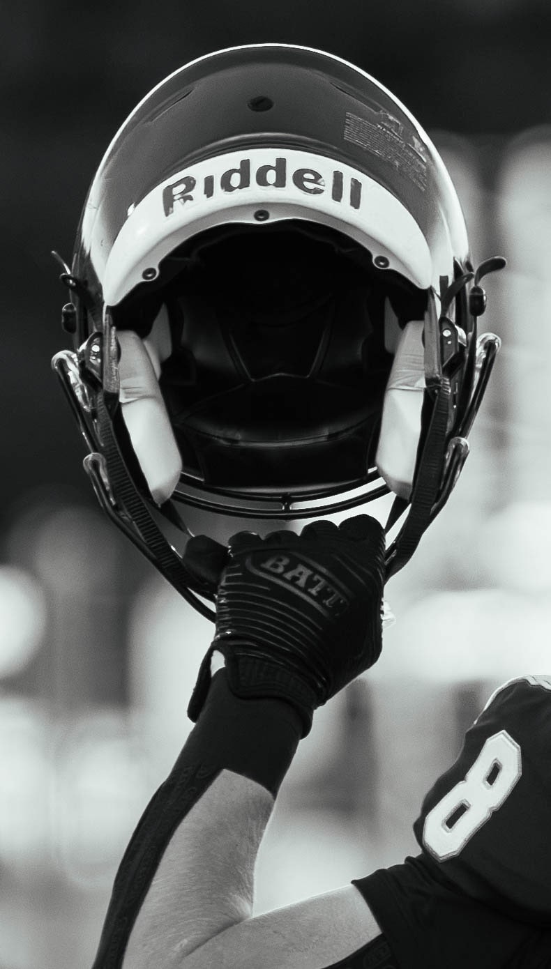 Black-and-white close-up of an East Lyme football player holding his helmet by the facemask