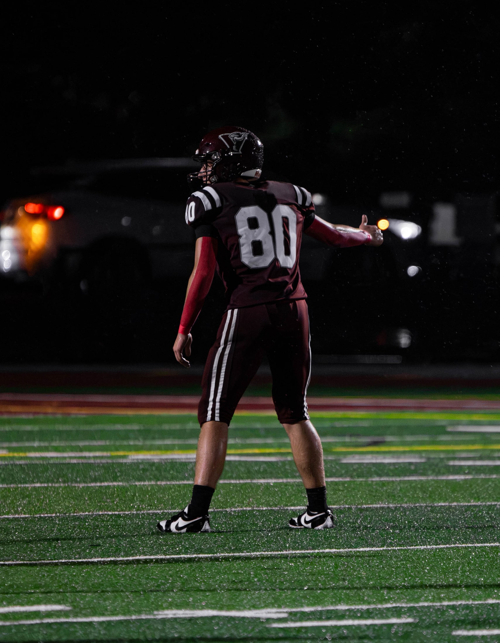 East Lyme number 80 signaling to teammates in the rain under the stadium lights